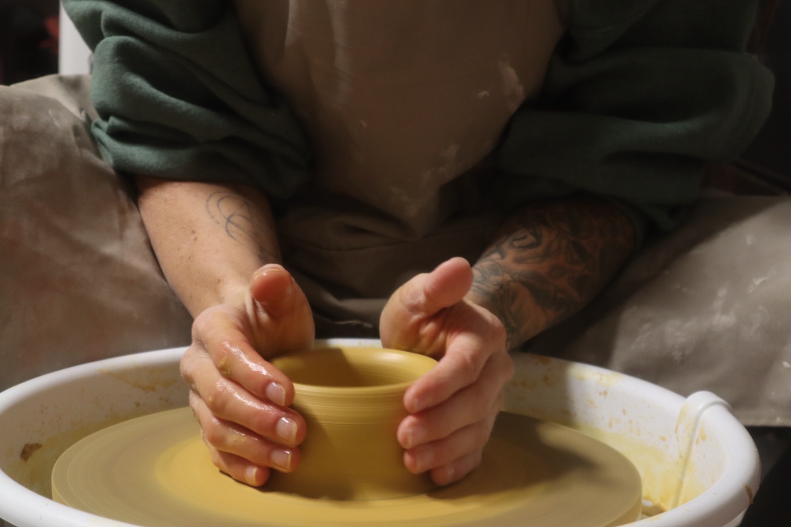 Hannah's hands shaping a clay cylinder on the wheel